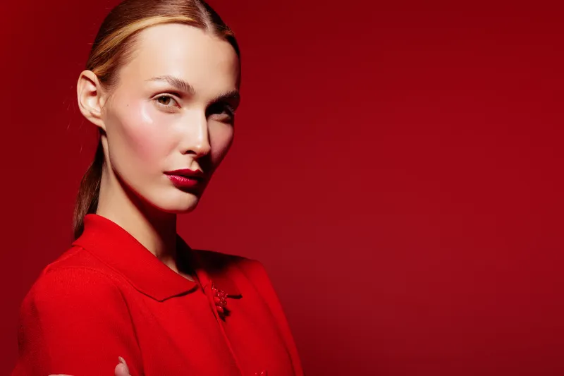 Young woman with red lipstick and red outfit poses confidently against red background. Concept of fashion, beauty, elegance, and bold style in studio lighting.