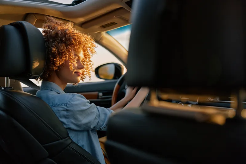 Woman lifestyle scene as she drives a car, relaxed and focused, daytime interior with sunlight, conveying independence and travel, candid portrait of everyday commuting and moments of calm
