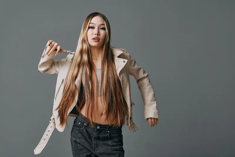 Young woman with long straight hair wearing beige jacket and black jeans posing on gray background. Fashion, style, beauty, lifestyle and casual portrait of confident girl.