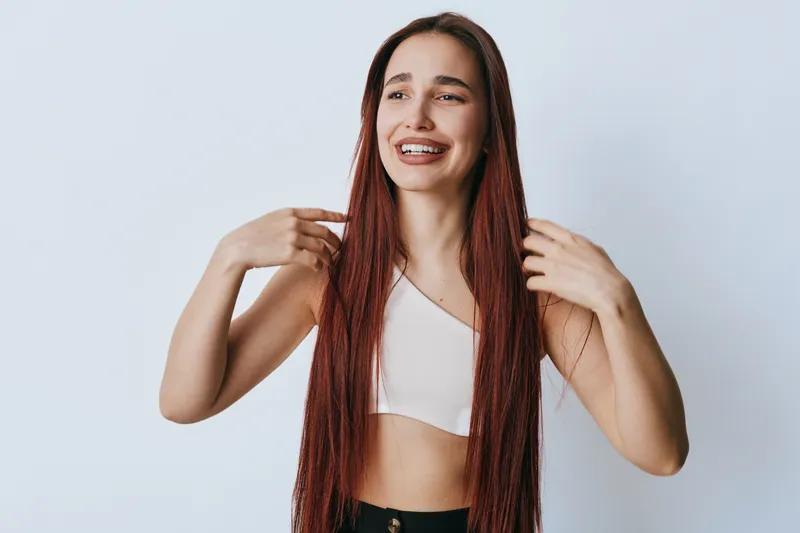 Young woman with long braided hair smiling and touching her hair on white background. Casual style, happy expression, beauty and wellness concept with natural look and confidence.