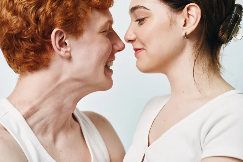 Young couple smiling and looking at each other closely in casual clothes with joy and affection in intimate moment on light background.