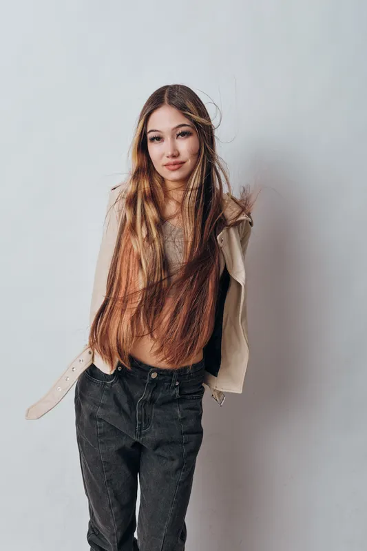 Young woman with long hair posing against light background wearing casual jacket and dark jeans confident and stylish female model with natural expression studio portrait.