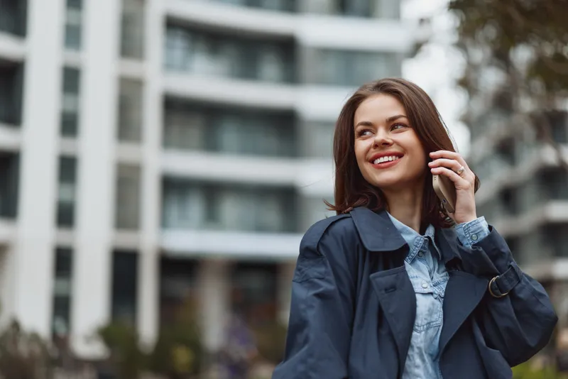 Smiling woman with brown hair wearing a denim shirt under a dark jacket in an urban setting, outdoor portrait highlighting fashion, confidence, and everyday style.