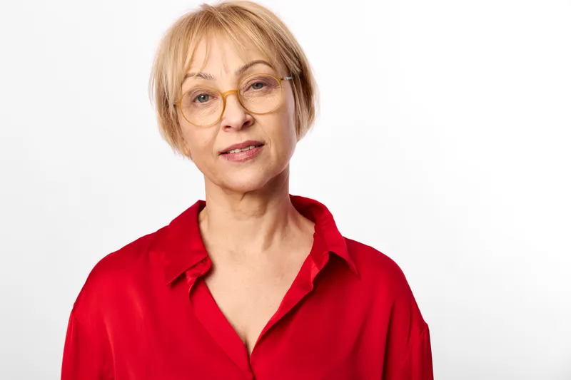 Woman portrait glasses red shirt female mature adult short hair on neutral studio background, calm gaze, closeup headshot, self confidence theme in lifestyle