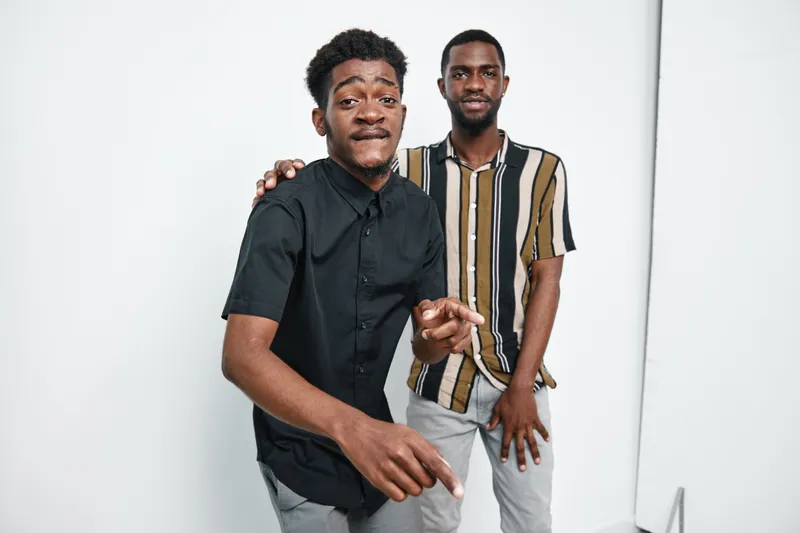 Two young black men with dark skin posing together in casual clothes on white background. Friends, portrait, smiling and standing close for lifestyle and friendship concept.