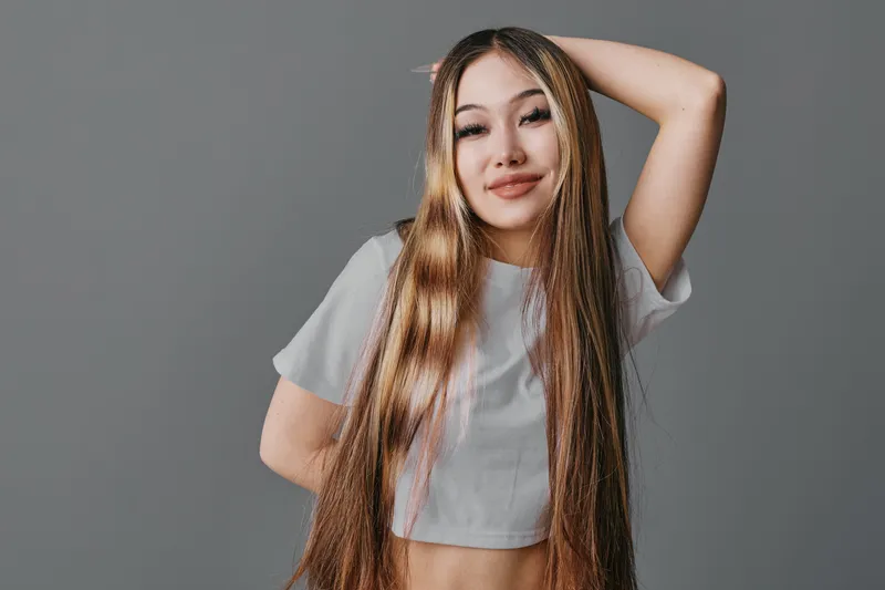 Young woman with long braided hair posing and smiling against gray background. Casual style, confident expression, and relaxed mood in studio portrait with t shirt.