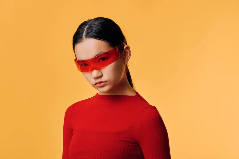 Woman with red sunglasses and red sweater posing on orange background, fashion portrait with minimal style, studio lighting and confident look for modern casual outfit.