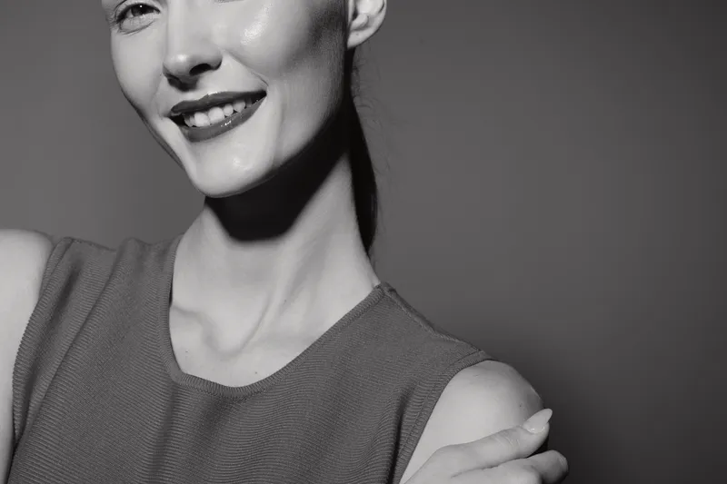 Close up of happy Asian woman with light skin smiling confidently in sleeveless top. Studio portrait with soft lighting and plain background. Concept of beauty, confidence, and positivity.