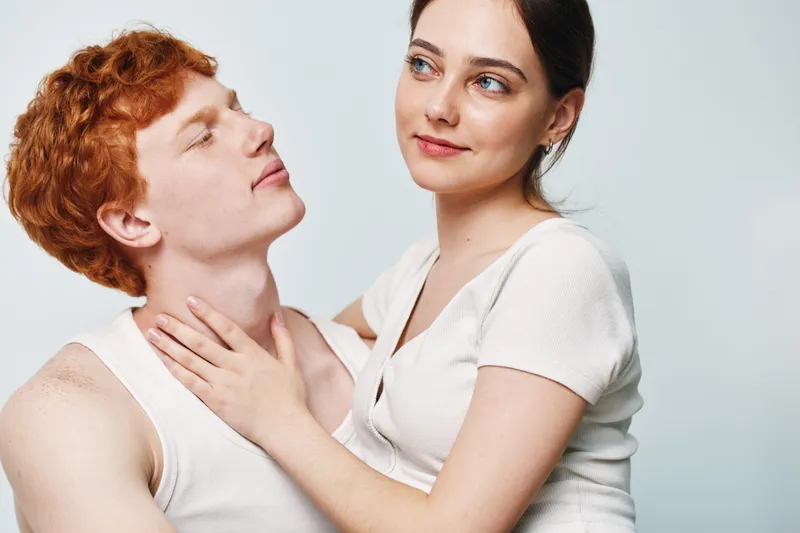 Couple, young man and woman, embracing and looking at each other with affection. Closeup portrait with casual clothing and soft expressions on light background.
