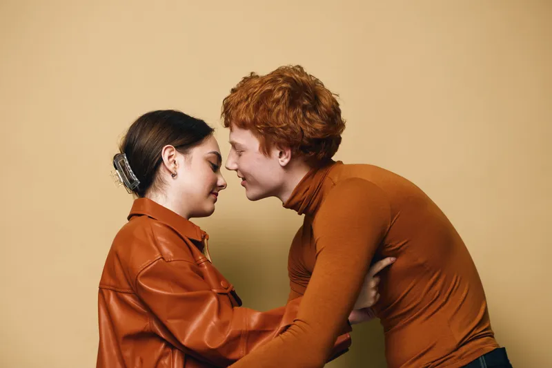 Couple, man and woman embracing with eyes closed in warm clothing against beige background. Intimate moment, affection and tenderness in indoor studio portrait with emotional connection.