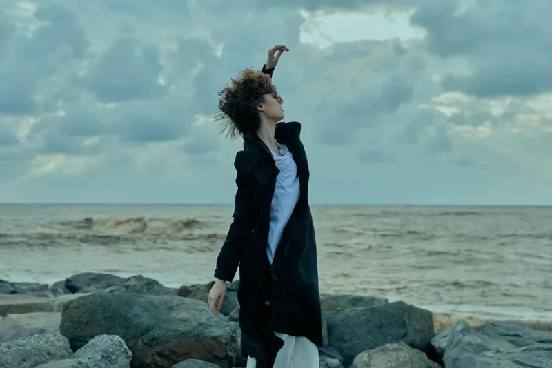 Fashion, woman, coat, sea, wind, outdoor, rocky, pose, scenery, photography on a windy coastline showing a stylish figure on a rocks edge with motion and coastal mood