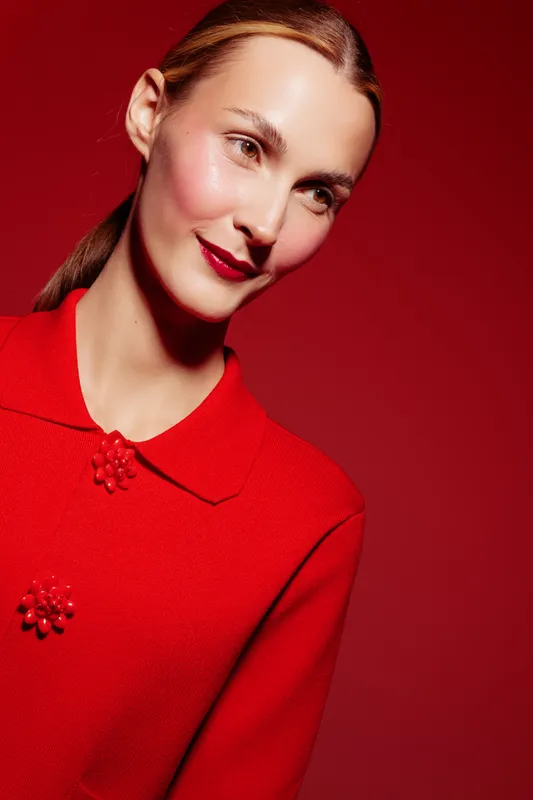 Portrait of a smiling woman with slicked hair wearing a red sweater against a red background. The image highlights fashion, beauty, and confident female model concepts.