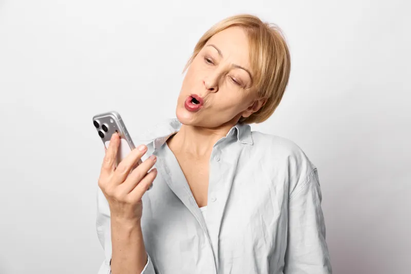 Woman with smartphone, surprised expression, wearing a light shirt, white studio background, communication and texting concept, modern technology, social media, mobile use