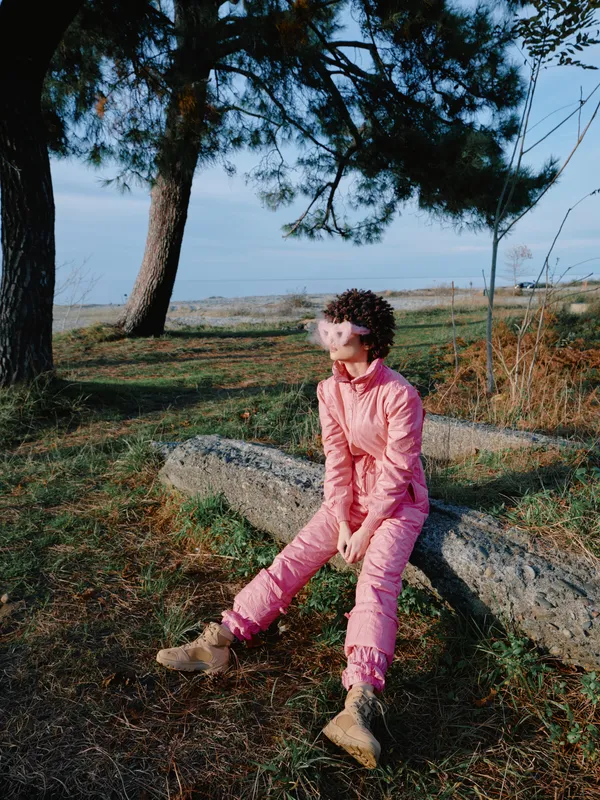 Child girl in pink jumpsuit sits on a stone in a park, outdoors among trees, a calm contemplative moment with natural light, casual fashion, childhood memory, scenic setting and relaxed pose