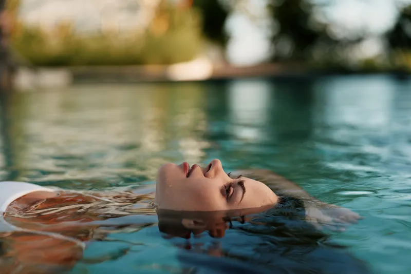 Young woman relaxing in swimming pool with eyes closed enjoying peaceful moment lifestyle concept summer leisure wellness and calm water background