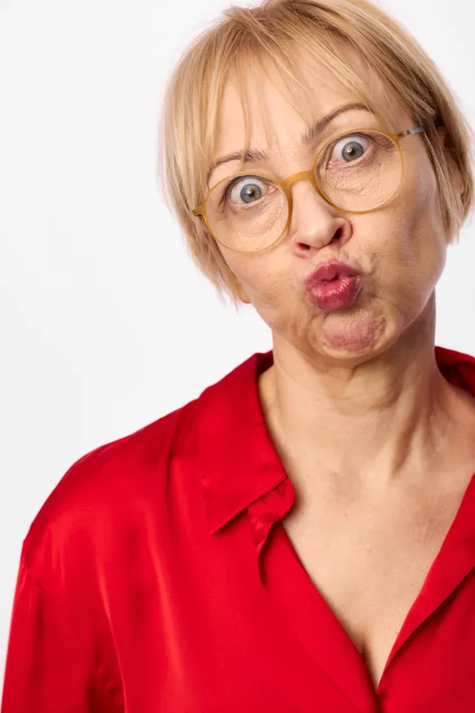 Woman portrait glasses surprised senior blonde red isolated white closeup, female headshot with round eyewear, amazed expression and open mouth, red blouse, studio background