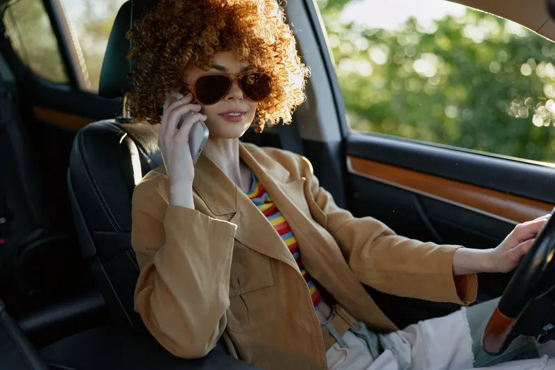 Candid woman in a vintage car, wearing a tan blazer and striped shirt. Close view of the seat and dashboard captures retro fashion and a relaxed lifestyle.