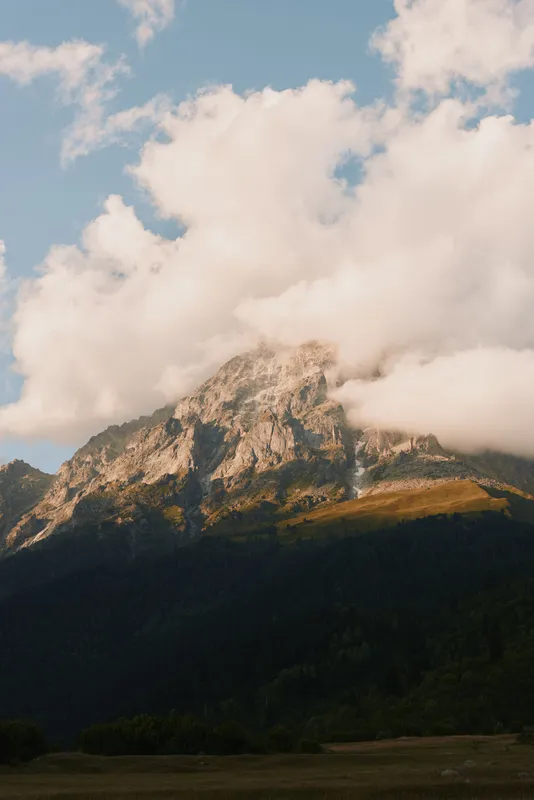 Majestic mountain peak covered with clouds during golden hour, natural landscape, serene atmosphere, soft light, clear sky, outdoor scenery, wilderness view