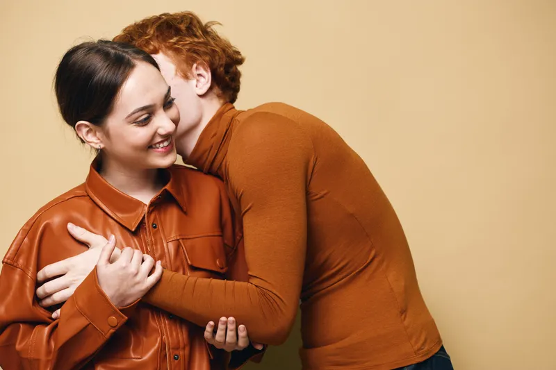 Couple embracing with affection and happiness in casual autumn clothes, expressing love and warmth in studio with beige background for relationship concept.