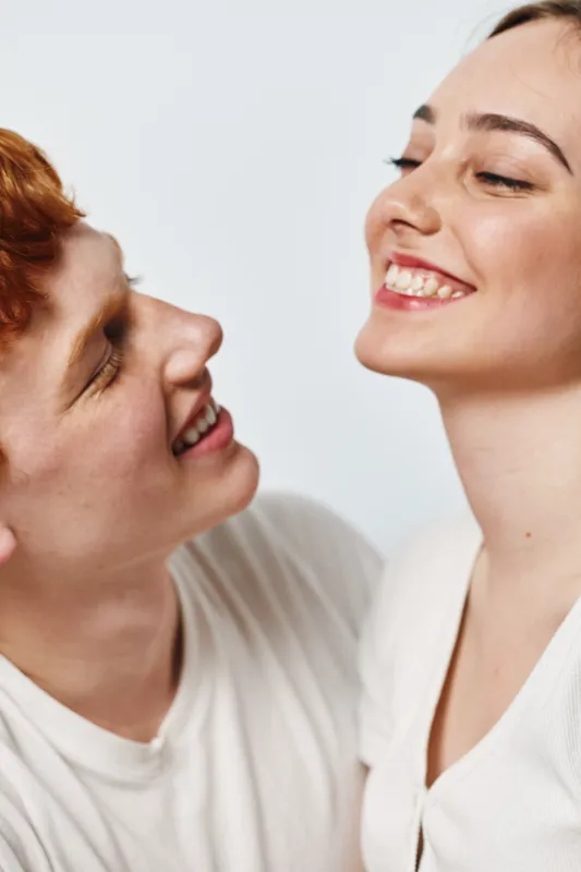 Smiling couple, young man and woman looking at each other with happiness, closeup portrait, light background, casual clothing, positive emotions and connection between them.
