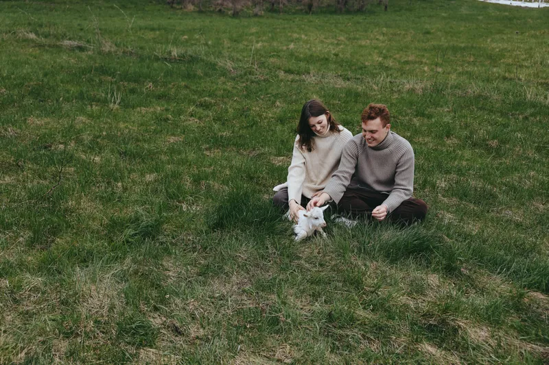 Goat kid with a couple in a grassy field outdoors, a natural lifestyle moment of bonding and nature, a serene pastoral scene highlighting companionship on an open pasture.