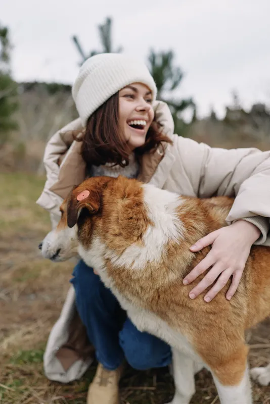 Woman outdoors hugs a dog with a joyful smile, capturing warmth, affection and nature on a chilly day in a candid, heartwarming moment