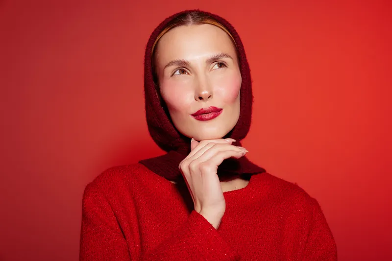 Portrait of a thoughtful woman wearing a red sweater and matching headscarf against a red background. Concept of fashion, style, and autumn mood with warm tones and soft lighting.
