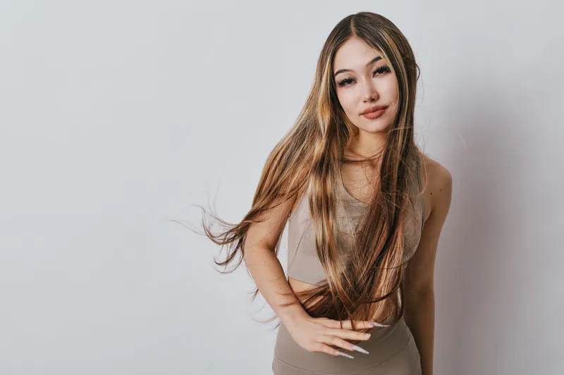 Young woman with long straight hair posing in casual beige outfit against white background. Beauty, fashion, confident female with natural makeup and natural hairstyle in studio setting.