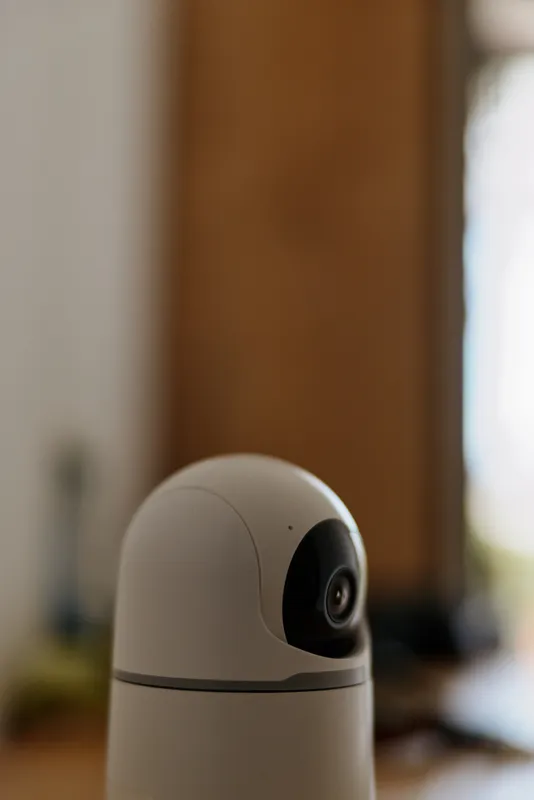Close up of a white home security camera on a soft blurred indoor background, conveying a calm vigilant mood