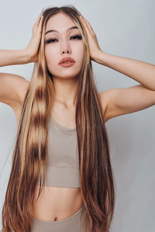 Young woman with long straight hair and hands on head posing against light background. Beauty, fashion and natural look with calm expression and casual clothing.