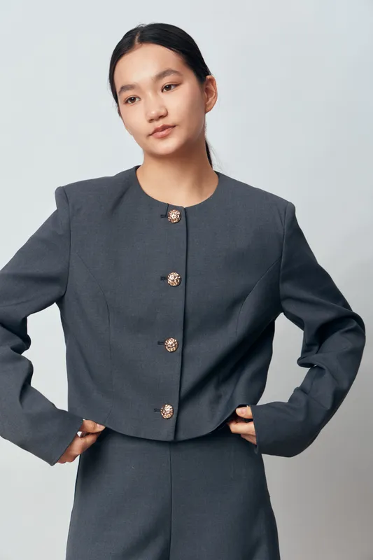 Young woman in grey tailored suit with decorative buttons posing for portrait on light background. Business style, confident model, fashion, elegance, formal wear and casual office look.