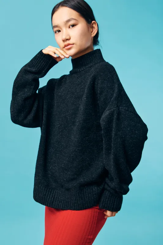Woman posing in black turtleneck sweater and red skirt on blue background. Fashion portrait, casual style, confident female model with natural makeup and dark hair pulled back.