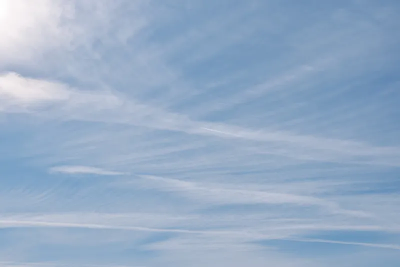 Blue sky with wispy white clouds spread across a bright daytime atmosphere, creating an expansive and serene background suitable for nature, travel, or design projects.