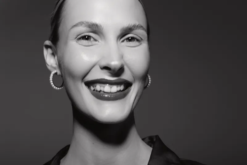 Happy white woman with pale skin and earrings smiles with teeth visible. Studio portrait in black and white. Concept of joy, beauty, and natural female expression.