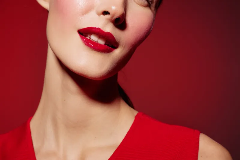 Close-up of a woman with red lipstick and smooth skin wearing a red dress against a red background. Concept of beauty, makeup, fashion, and elegance with vibrant colors.
