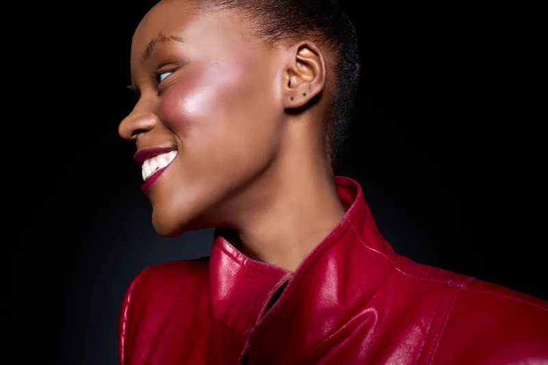 Profile of a smiling black African woman with dark skin wearing a red leather jacket against black background. Concept for beauty, fashion, confidence, and style portrait.