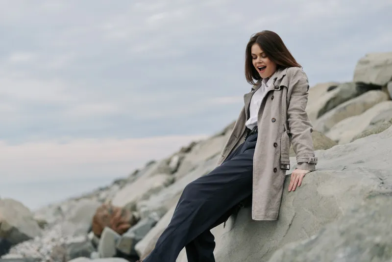 Young woman in casual clothes sitting on large rocks near the sea, enjoying fresh air and nature. Cloudy sky creates calm and relaxed mood in outdoor setting.