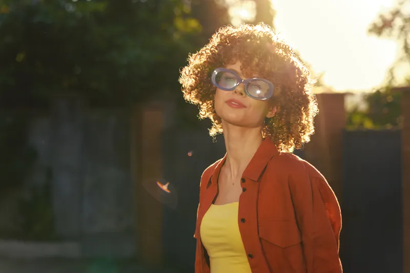 A stylish woman enjoys sunny outdoor life, wearing sunglasses, a yellow top and red shirt, posing confidently in a bright setting. A candid portrait for modern lifestyle