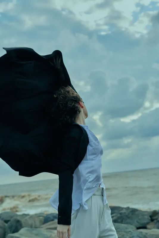 Windy seaside scene with flowing coat and moving fabric, outdoor motion by the shore with calm ocean and dramatic mood