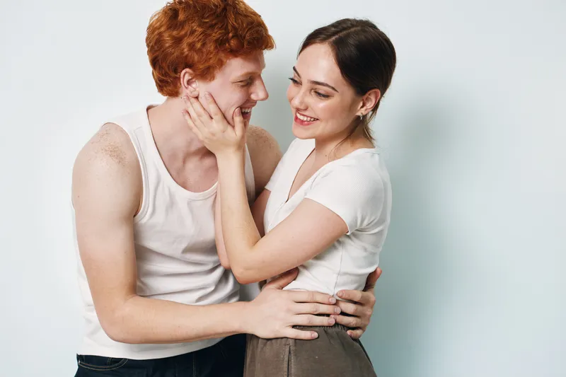 Couple, love, affection, smiling, young man and woman in casual clothing embracing and looking at each other on white background, happy relationship and intimacy moment.