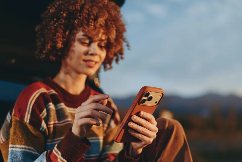 Woman lifestyle smartphone outdoors curly hair mountains sunset young woman with curly red hair holds two smartphones smiling during golden hour with distant mountains and open sky