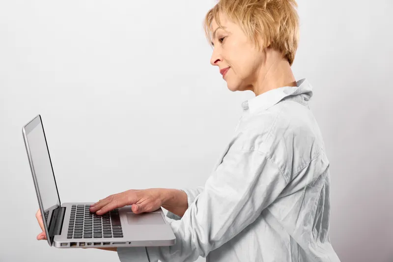 Woman typing on a silver laptop in side view, clean white studio background. Concept of remote work, business communication, technology, focus intently.