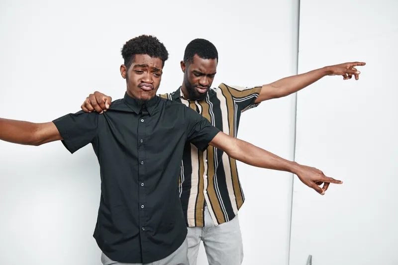 Two African American men with dark skin posing and pointing in different directions in casual clothing on white background for friendship and fun concept.