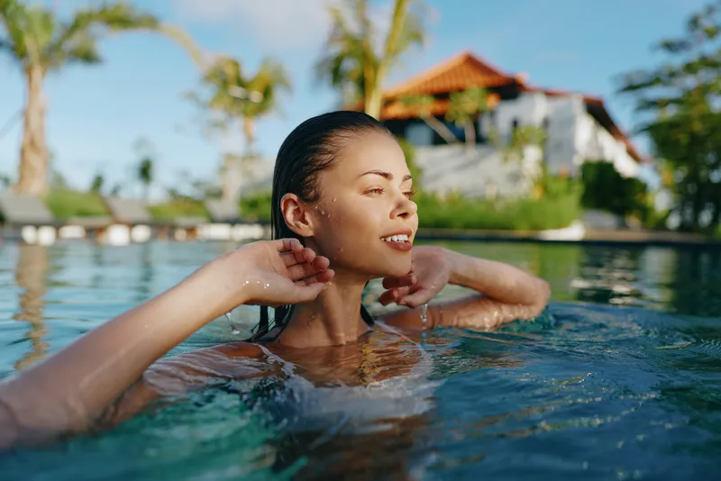 Relaxed woman enjoys a pool during vacation in a tropical setting, water and sun create a serene moment of leisure and renewal by clear blue water