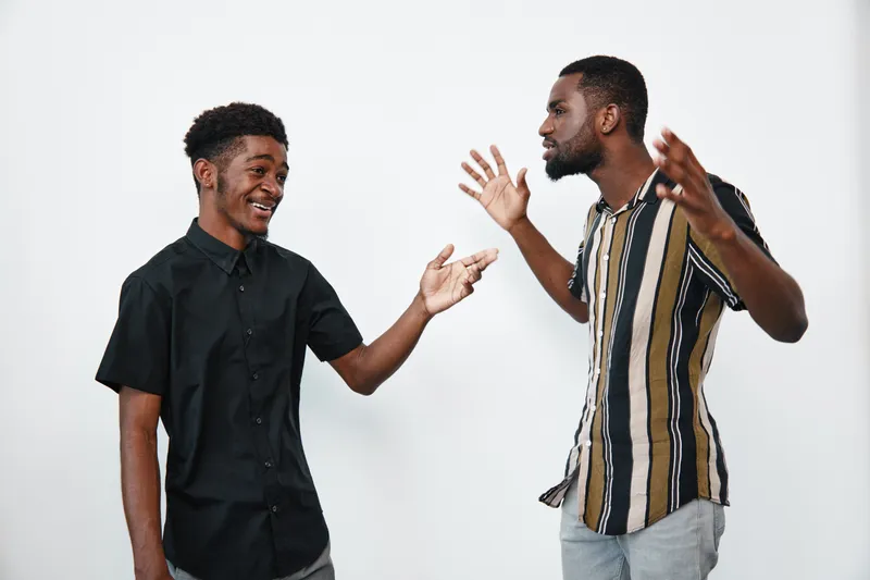 Two African American men with dark skin having a lively conversation and smiling in casual clothes against white background. Friendship, communication and positive interaction.