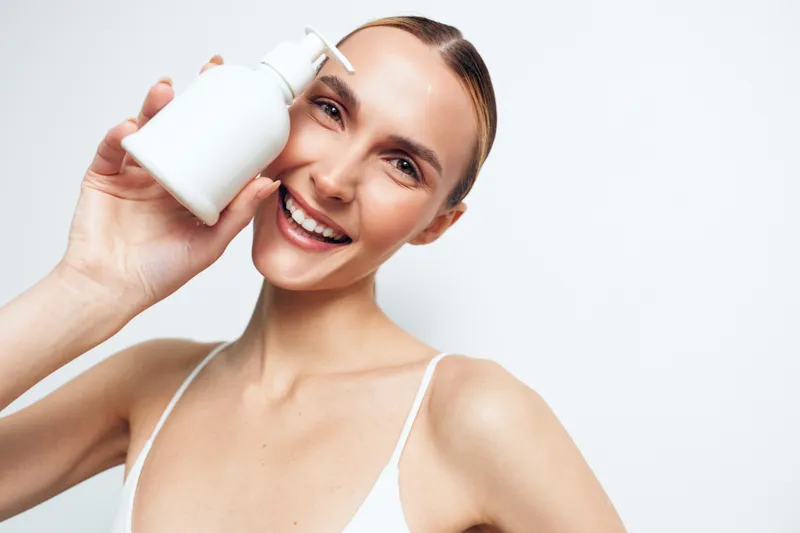 Smiling woman holding milk bottle near face, close up beauty and skincare concept, dairy nutrition for healthy skin, clean white background, bright natural light, soft glow