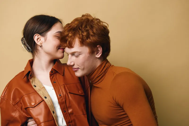 Couple, love, intimacy, affection and relationship with smiling woman and man gently embracing with closed eyes in warm clothes and neutral background indoors.