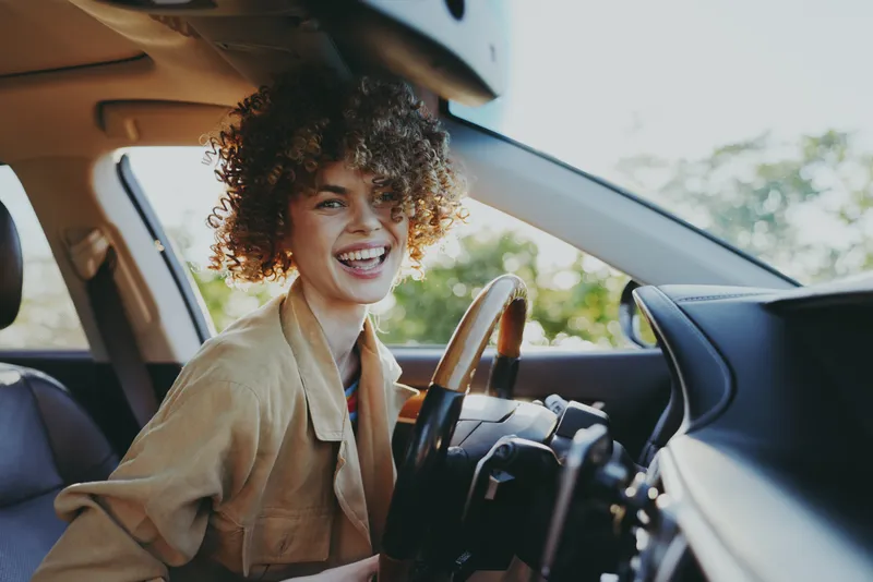 woman lifestyle portrait inside car, smiling softly in candid moment, retro film color vibe, warm sunlight and relaxed mood soft breeze through window adds depth, natural colors.