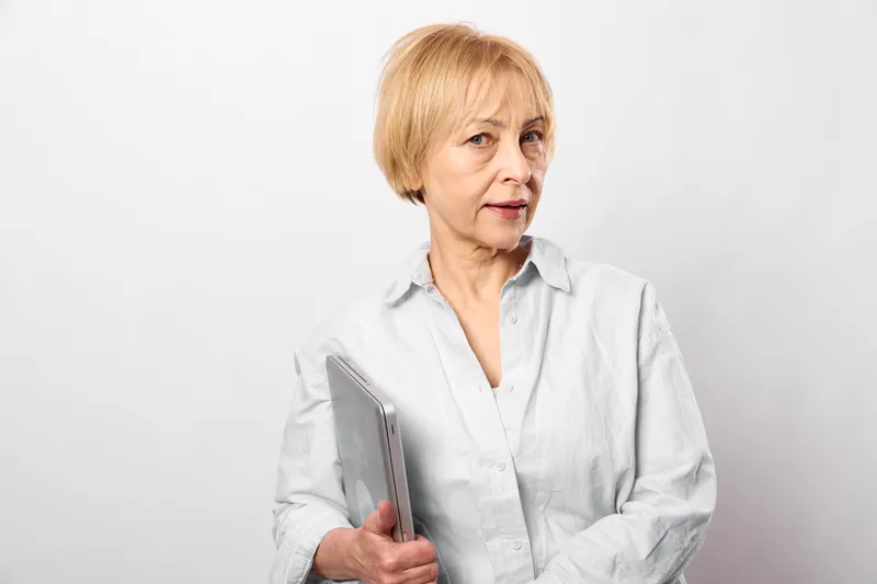 Elderly woman holding smartphone, studio portrait with white background, looking at camera, technology and communication concept, indoor calm mood today