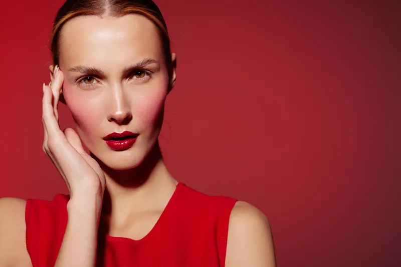 Portrait of a confident woman with red lipstick and red dress posing against a red background. Concept of beauty, fashion, makeup, and elegance with strong color contrast.
